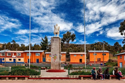 Central square with stone monument, colorful houses and people on benches, cloudy sky, Great Inca