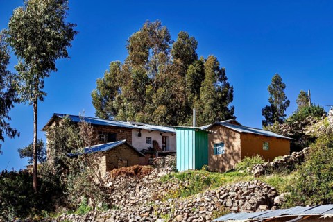 Small rural farm houses and tall trees on a rocky hill under a clear sky, the countryside and