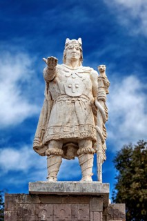Stone statue of a warrior with a raised hand against a blue sky, Great Inca monument on Taquile