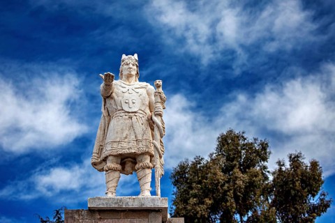 Stone statue of a warrior against a cloudy, blue sky, Great Inca monument on Taquile Island in Lake