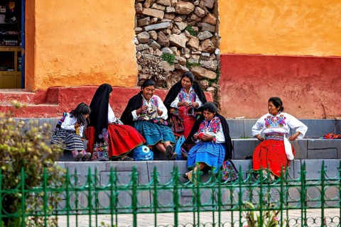 Group of woman in colorful traditional clothing sit on stairs and talk vividly, the woman on
