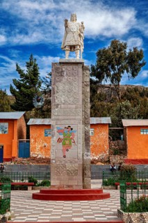 Stone figure and reliefs in front of colorful houses under blue sky, quiet environment, Great Inca