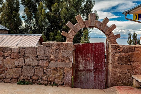 Stone wall with wooden gate and views of sky and nature, stone gates on the island of Taquile in