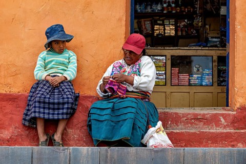Two woman in traditional clothes sit on a staircase next to a small shop, The woman on Taquile