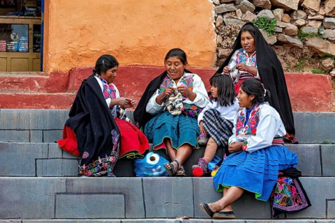 Women and children in traditional clothing sit on steps and interact with each other, the woman on