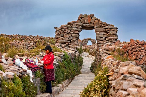 Woman next to clothes on traditional path with stone walls, stone gates on Taquile Island in Lake