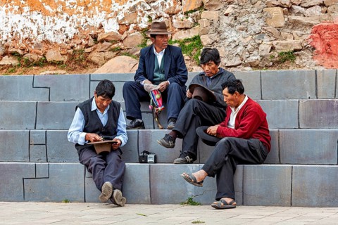 Four men in traditional clothing sit relaxed on stone steps in an urban setting, men sit together