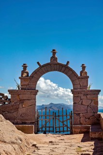 A stone archway with decorations that opens up to a vast mountain panorama under a blue sky, stone