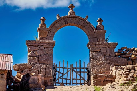 Massive stone archway with decorated sculptures rising into a clear blue sky, stone gates on