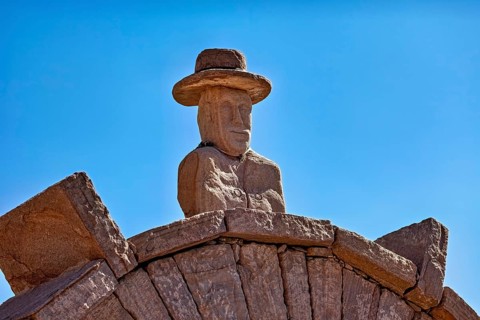 Stone bust with hat on an archway, artfully designed against a clear blue sky, stone gates on the