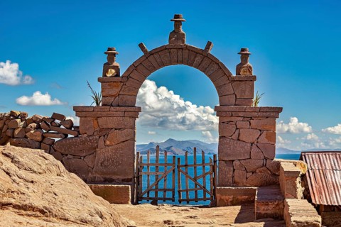 A traditional stone arch with wooden slats stands in front of a distant mountain landscape under