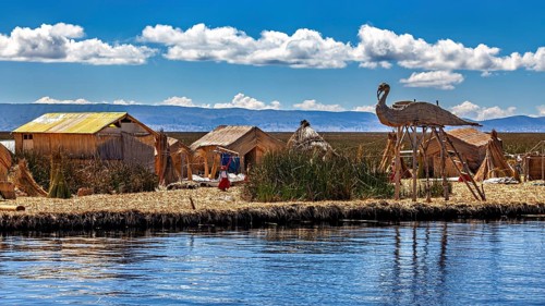 Handmade huts with thatched roofs and boats on the edge of a lake under a cloudy sky, The floating