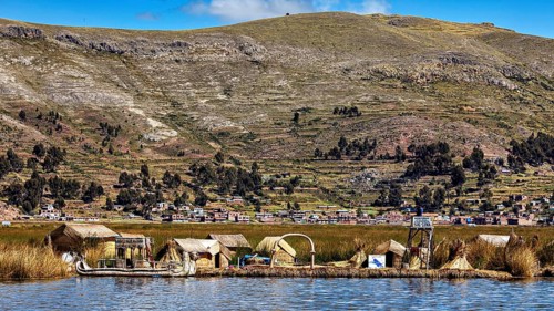 Small reed village on the shore with mountains in the background under a blue sky, The floating