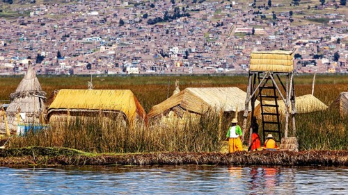 Small village of reed huts with people on the shore in front of an extensive urban landscape, The