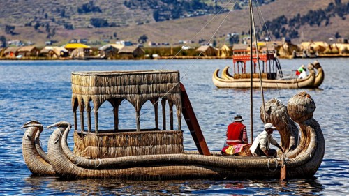Traditional reed boat with people on a calm lake in front of a shore with reed huts, The floating