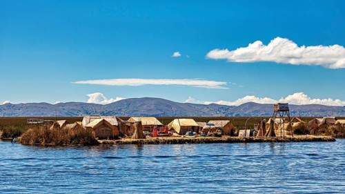 Reed huts on an island in the lake under a clear sky with mountains in the background, The floating