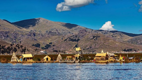 Small reed settlement on a lake against a mountain backdrop under a cloudy sky, The floating reed