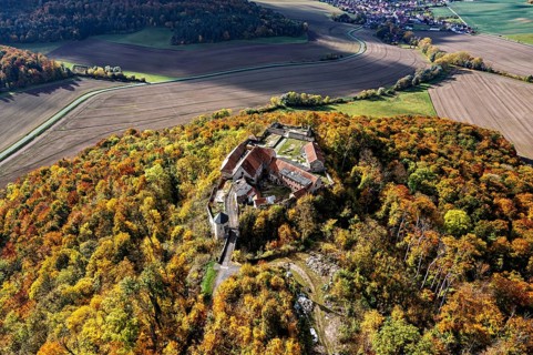 Aerial view of a castle on a hill surrounded by autumnal forest with colorful trees, Gleichenstein