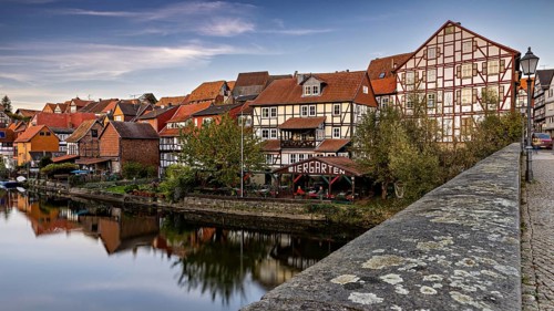 Historic half-timbered houses and beer garden along a river with a bridge at dusk, The town of Bad