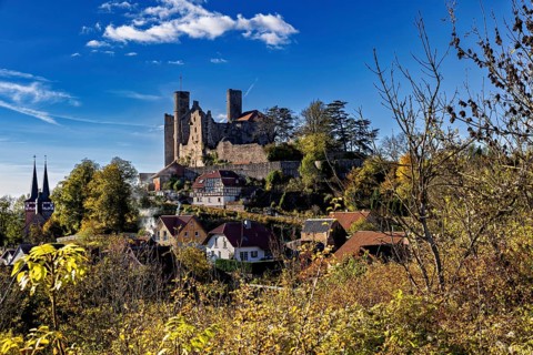 Castle above a village with a church, surrounded by autumn trees under a blue sky, Hanstein Castle