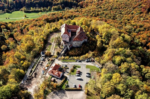 Castle taken from the air in the midst of autumn nature, with adjacent parking facilities,
