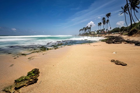 Sunny Kauam beach with palm trees, endless ocean, rocks and waves under a blue sky, Koggala beach
