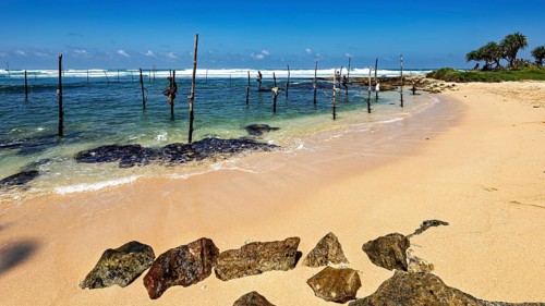 Quiet beach with clear waves and wooden poles under blue skies, Koggala beach with stilt fishermen