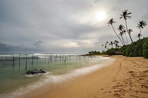 Tropical beach with soft waves, palm trees and cloudy sky, Koggala beach with stilt fishermen in