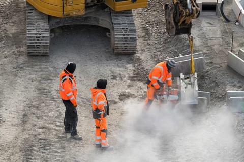 Construction workers in protective clothing work with machines on a dusty construction site,