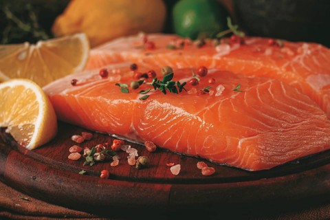 Two salmon fillets rest on a wooden platter. The fillets are garnished with herbs and spices. Lemon
