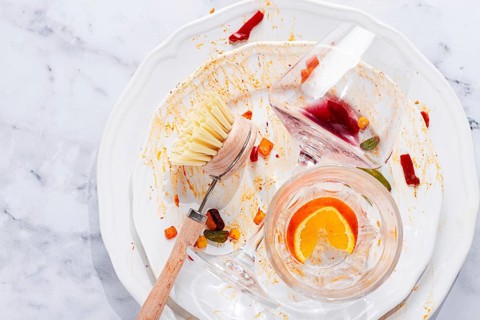 Dishes are stacked on a kitchen counter with food remnants after a meal. A cleaning brush and