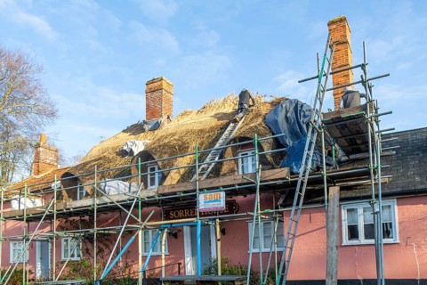 Thatcher at work replacing thatch ridge of thatched country pub building, Sorrel Horse, Shottisham,