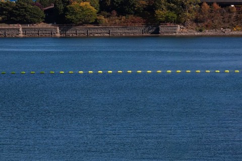 String of yellow cautionary navigation marker buoys on water surafce of river serving to warn,