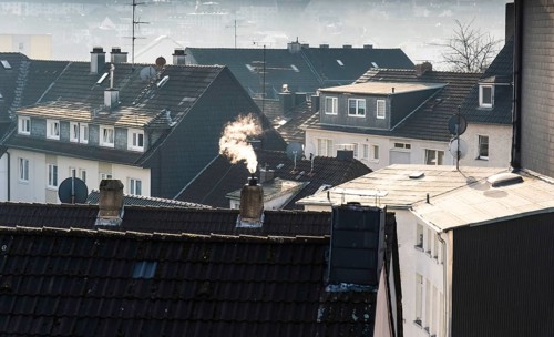 Smoke plume from a chimney over densely built residential area in the evening light, wintry city