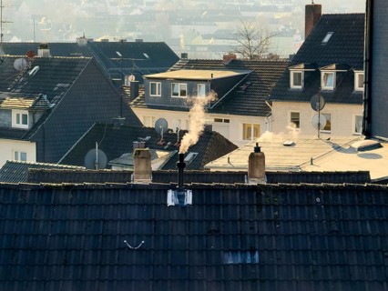 Smoke plume from a chimney over densely built residential area in the evening light, wintry city