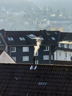 Smoke plume from a chimney over densely built residential area in the evening light, wintry city