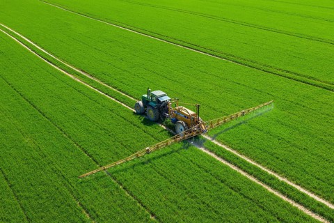Aerial view over agricultural trailed field sprayer pulled by tractor spraying crop on farmland,