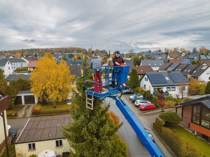 View of workers in a lift in front of a panorama of an autumnal residential area, tree work,