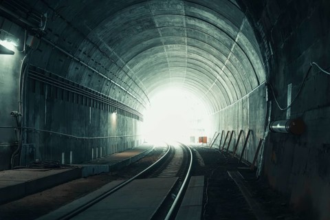 An illuminated tunnel with railroad tracks and a bright exit, acceptance of the Hermann Hesse