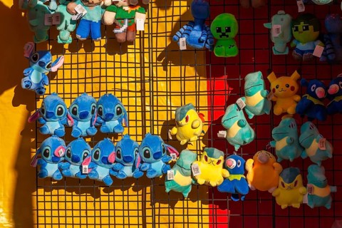 Close-up of blue, yellow and green plush prize dolls at game kiosk at Fun Show traveling ride park,