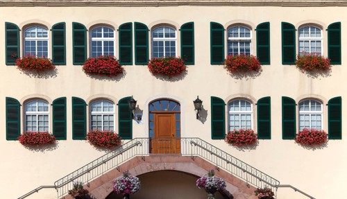 Architectural façade with symmetrical windows and green shutters decorated with red flowers, Bad