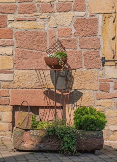 Rustic iron decoration on a stone wall, clay pot with plants in sunshine, Palatinate,