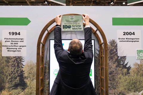 A stand operator hangs up a sign Congratulations to Messe Berlin on 100 years of Green Week at the