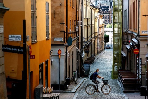 A cyclist in a picturesque old town alleyway in Stockholm, surrounded by charming buildings,