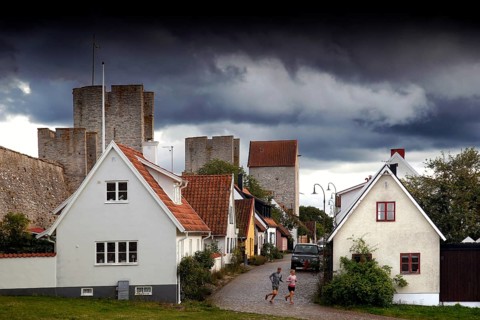 Alley in Visby's old town with historic buildings and city wall towers under a dramatic sky, Visby,