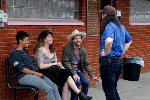 Four people sit relaxed in front of Fred's Lounge and laugh together, Mamou, Louisiana, USA