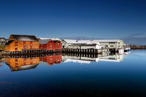 Warehouses in Vardø harbour are reflected in still water, Vardø, Finnmark, Norway