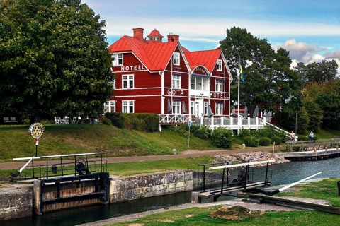 Red Göta Hotel in Borensberg on the Göta Canal next to a lock, surrounded by green trees,
