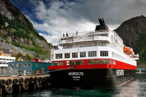 Hurtigruten ship in harbor with surrounding buildings and mountainous landscape, Øksfjord, Norway