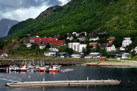 Quiet harbor with small boats and surrounding colorful houses in mountainous landscape, Øksfjord,